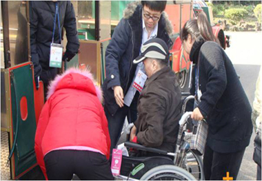 여행사 직원 및 요양보호사들이 이동차량에 오르는 휠체어에 탄 어르신을 돕고있다.